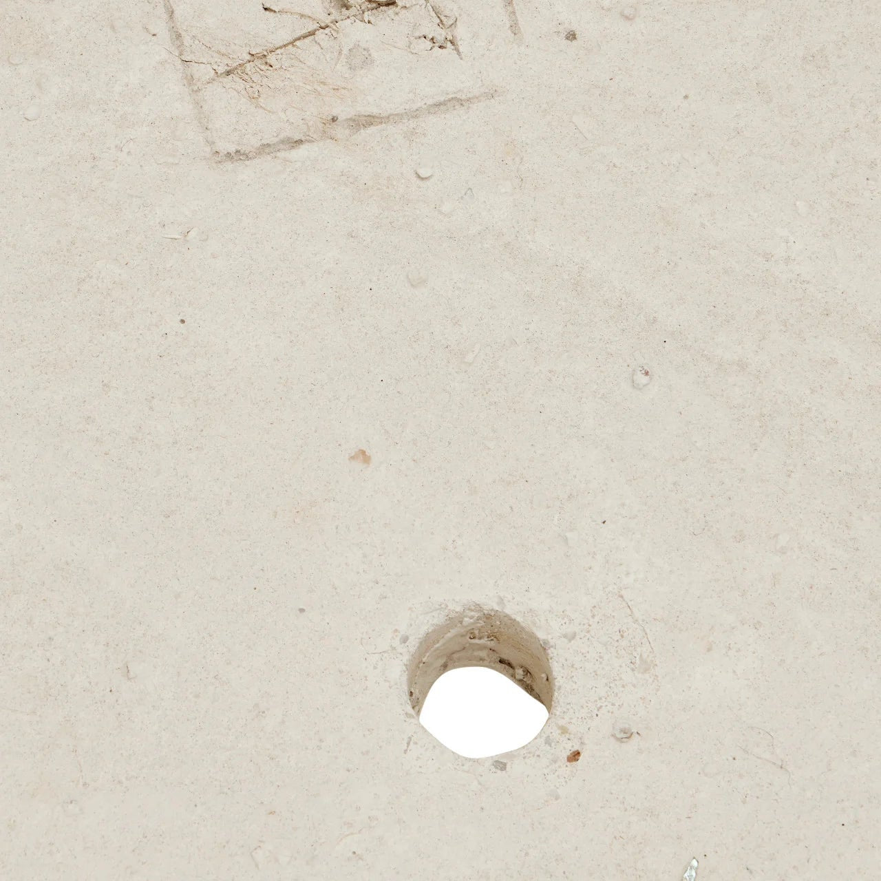 A close-up of a light beige textured surface with a small circular hole near the bottom center and a faint stamped square mark near the top left.