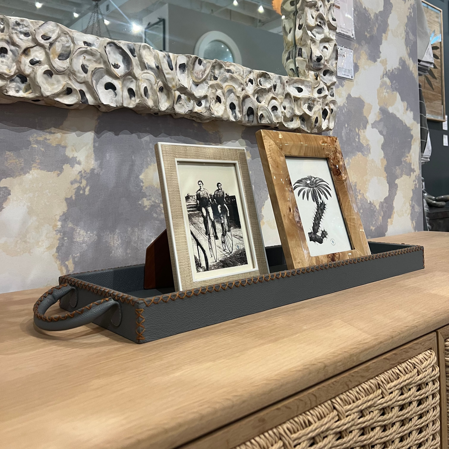 Decorative mirror with textured frame above a wooden surface with framed pictures.