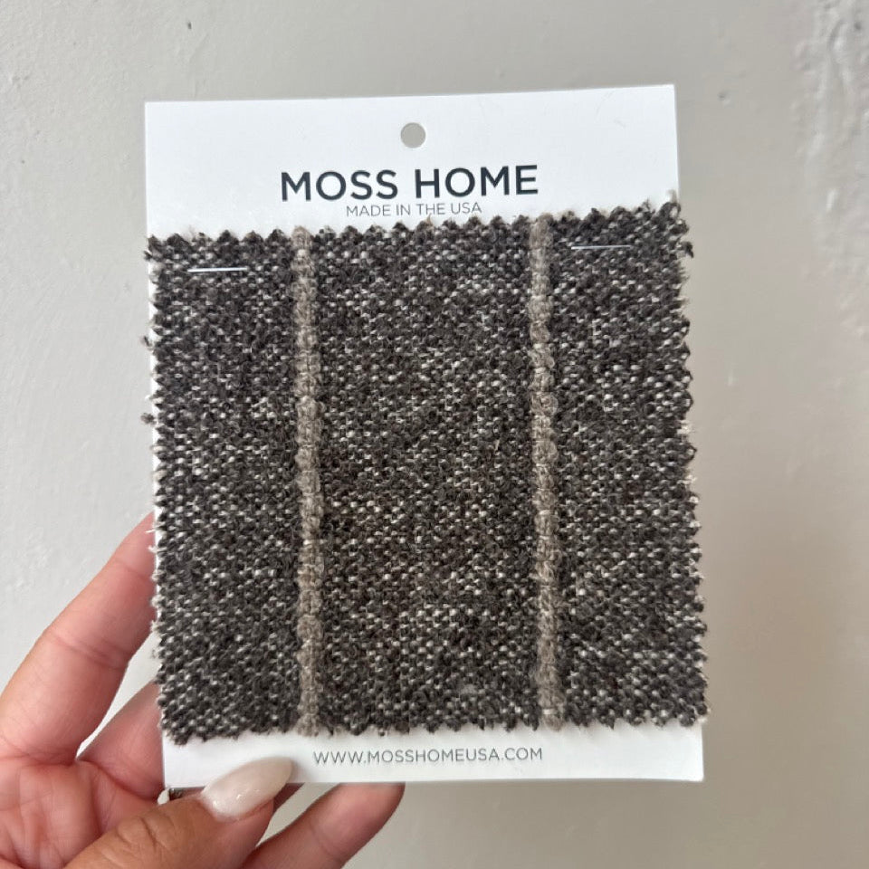 Moss Home fabric sample card held by a hand against a gray background
