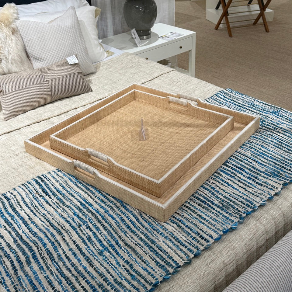 Wicker tray on a bed with pillows and a lamp in the background