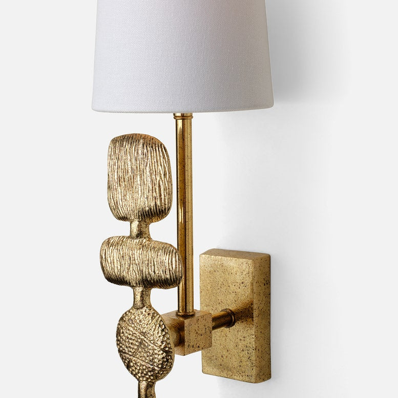 Decorative wall sconce with textured gold base and white shade on a light gray background