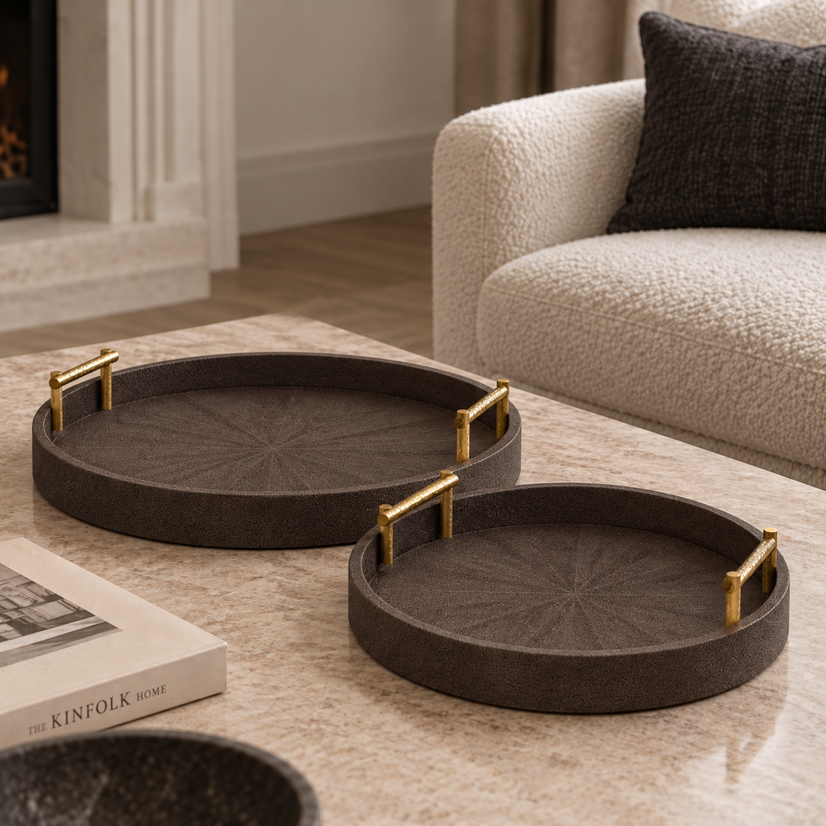 Two round dark brown woven tray coasters with gold metal corner accents resting on a light marble coffee table in a modern living room setting.