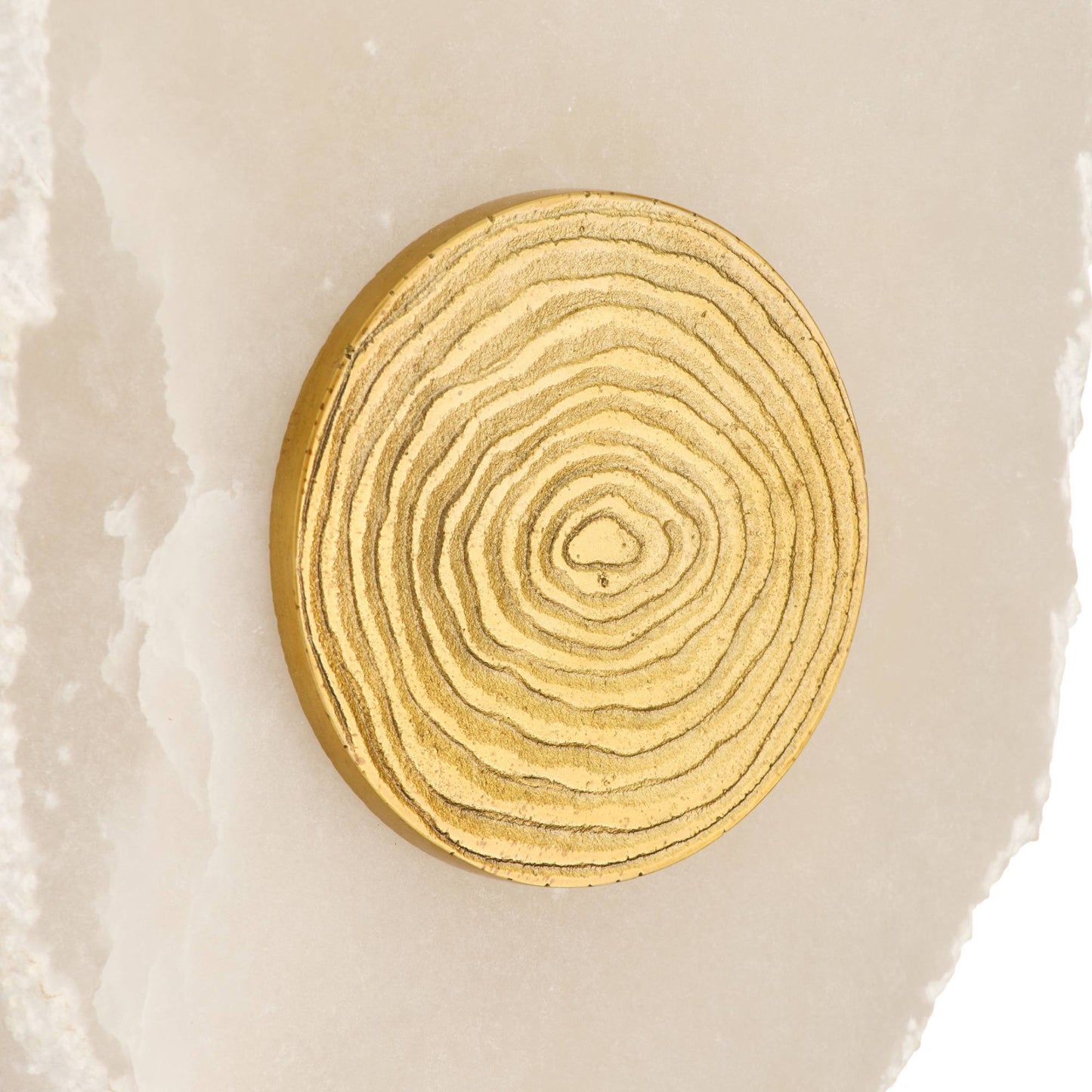 A round gold-toned wall plaque featuring concentric wood grain rings, displayed on a light beige stone surface.