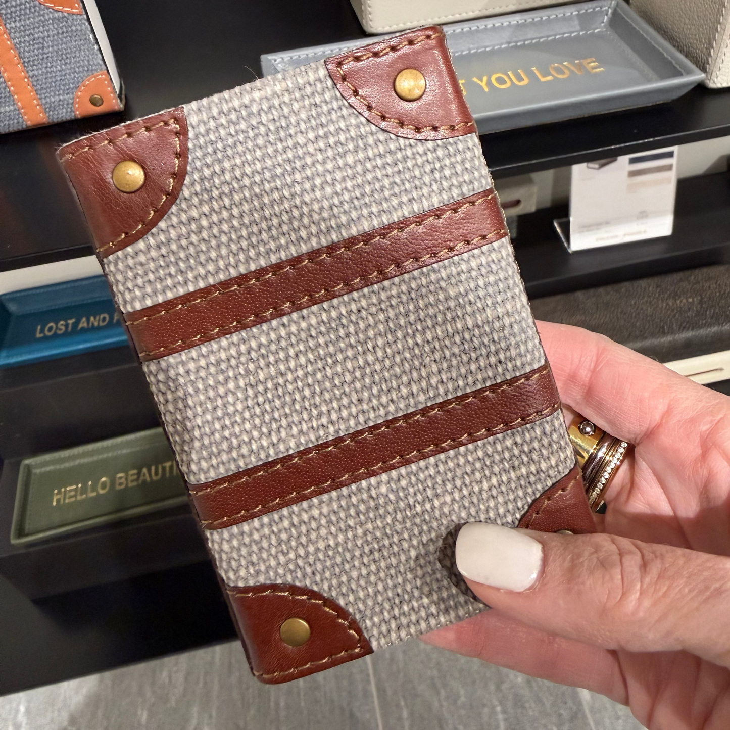 Hand holding a fabric phone case with brown leather accents in a store setting.