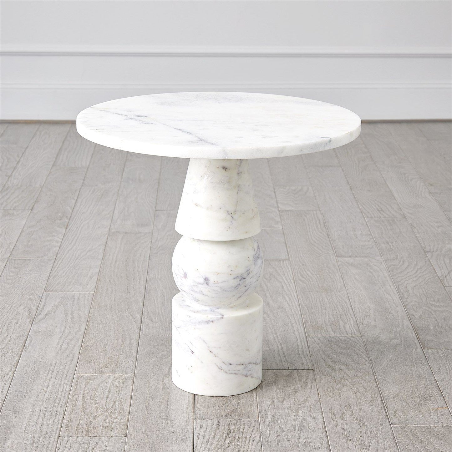 Marble dining table with stacked cylindrical legs on a wooden floor.