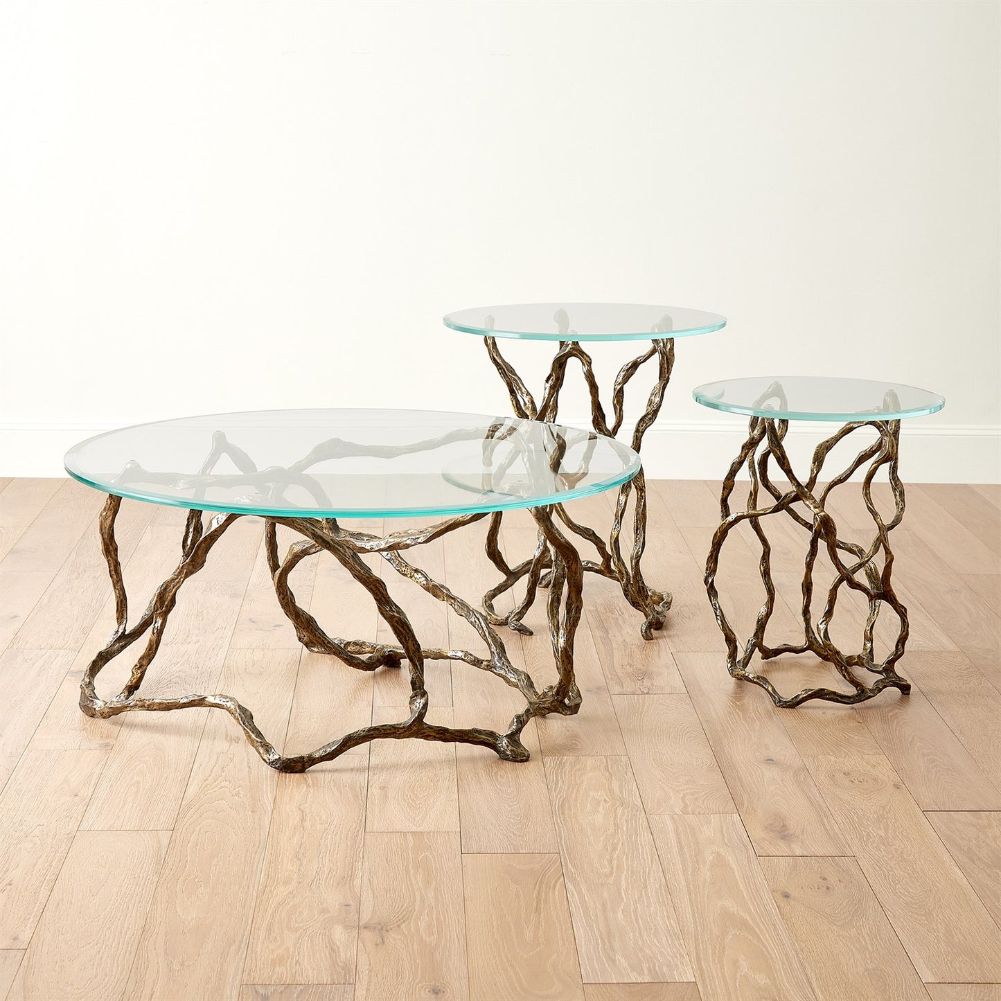 Set of glass tables with natural branch-like bases on a wooden floor.