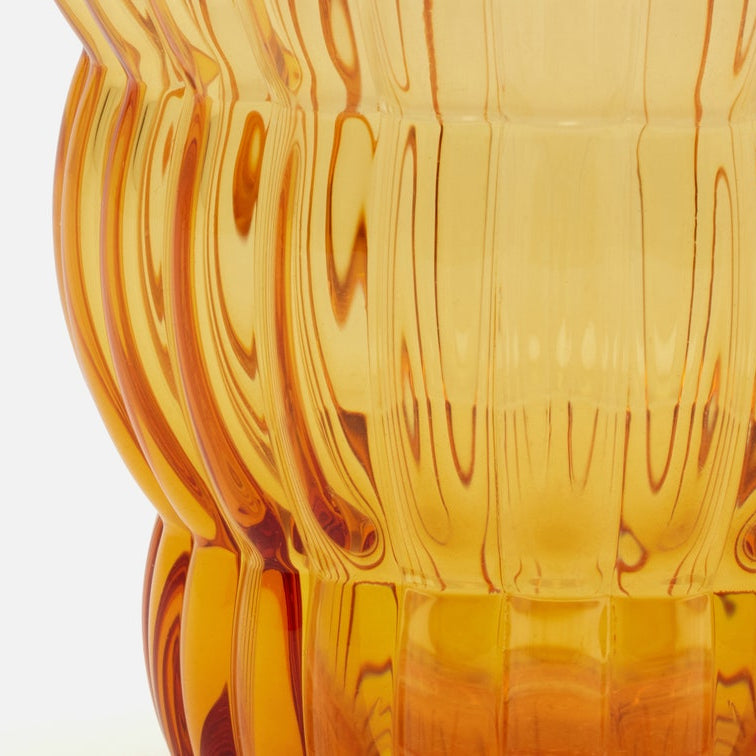 Close-up of a translucent amber glass vase with a fluted, ribbed texture and warm golden-orange tones against a white background.