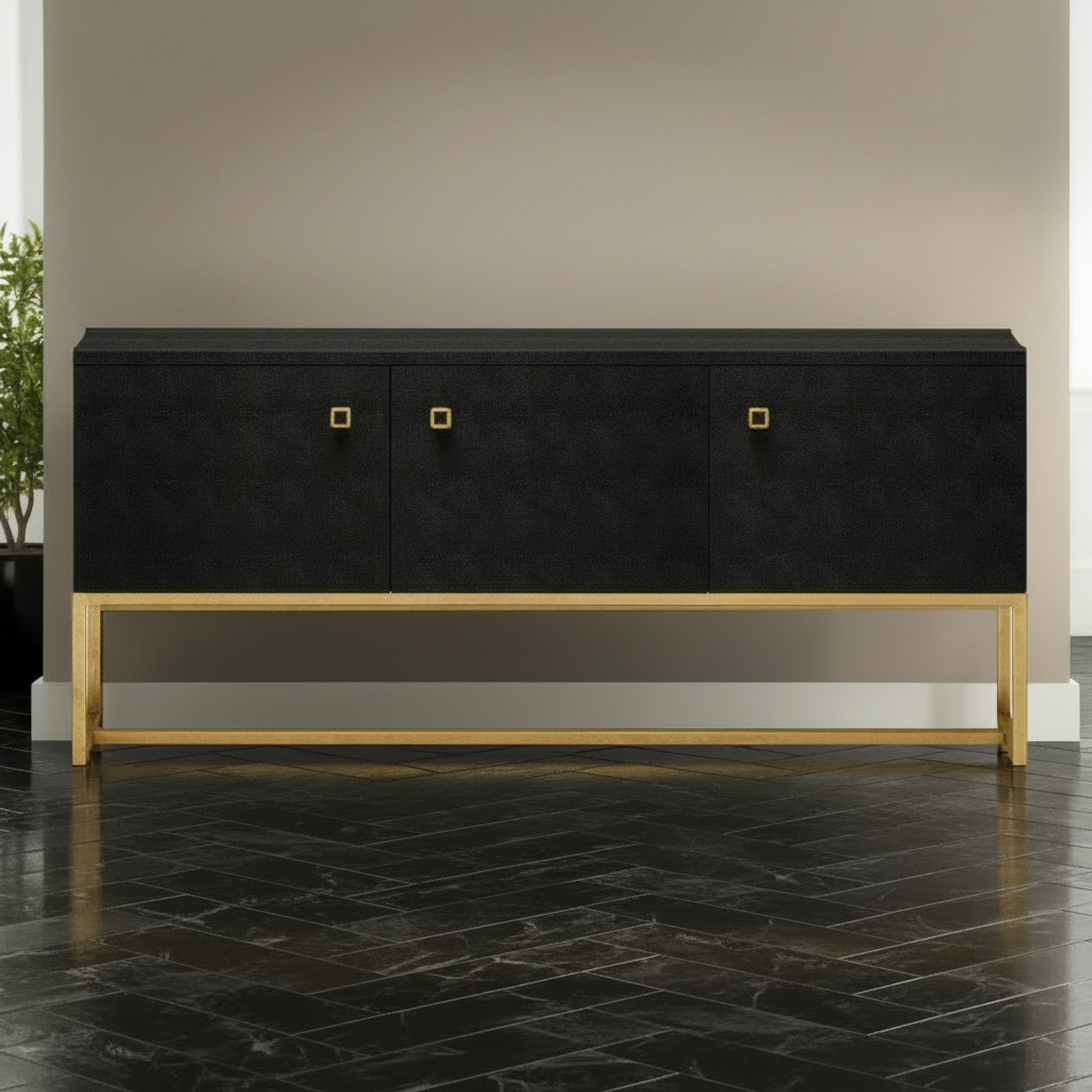 A modern black sideboard or credenza with a textured finish, featuring three doors with small gold square handles and a gold metal frame base, set against a neutral interior background.