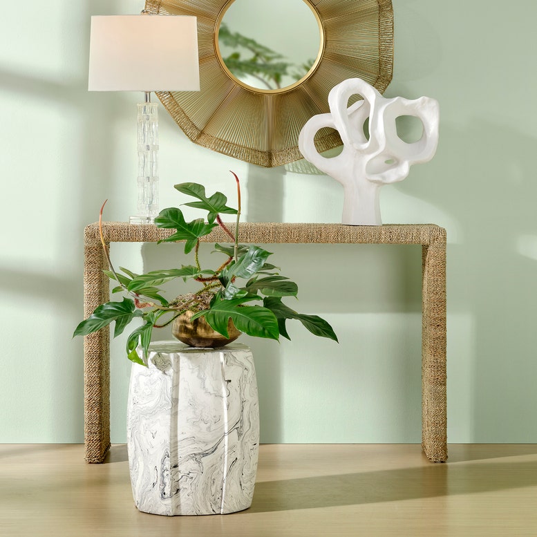 Decorative table with a plant, vase, and abstract sculpture against a light green wall.