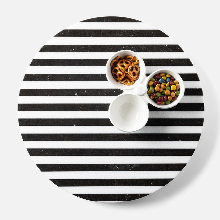 Round black and white striped tray with small bowls of snacks on a light gray background