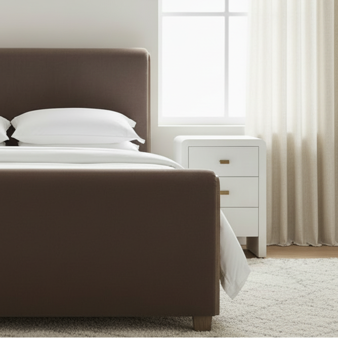 Bedroom with a bed featuring a brown upholstered headboard and white bedding, next to a white nightstand. sloane bed