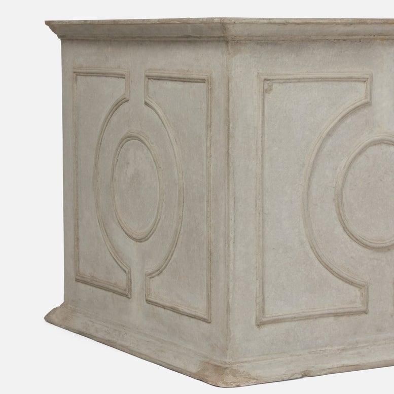 A close-up of a light gray stone or concrete planter box with decorative embossed panel designs on a plain white background.