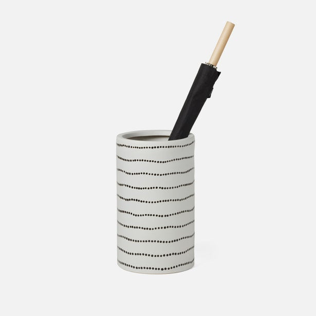 White cylindrical container with black dot pattern holding a black umbrella on a white background