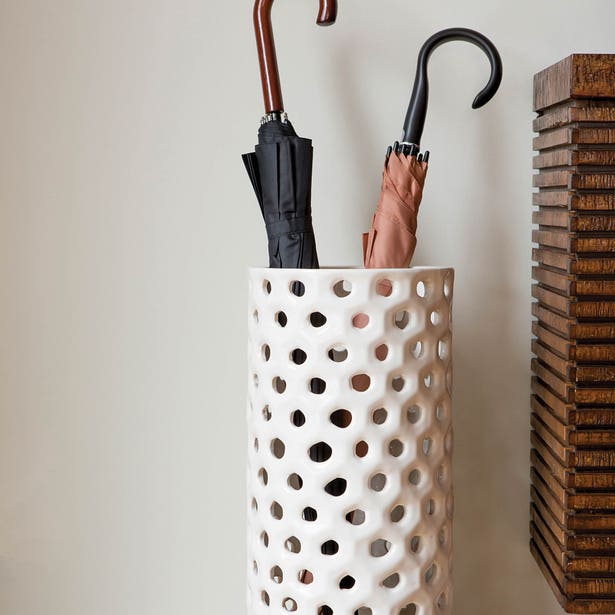 White perforated umbrella stand holding three umbrellas against a neutral background