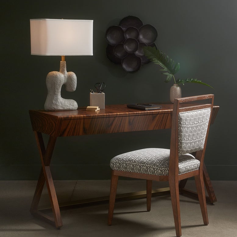Wooden desk with chair, lamp, and decorative items against a dark wall.
