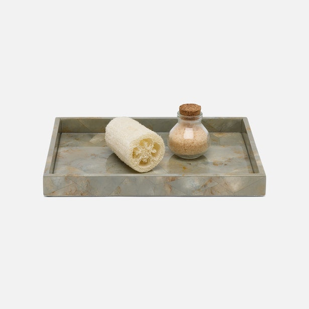A rectangular stone tray with a gray and beige marble pattern, styled with a natural loofah sponge and a small glass bottle with a cork stopper containing bath salts, set against a plain light gray background.