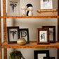 Decorative wooden shelf with framed pictures, sculptures, and a gold vase.