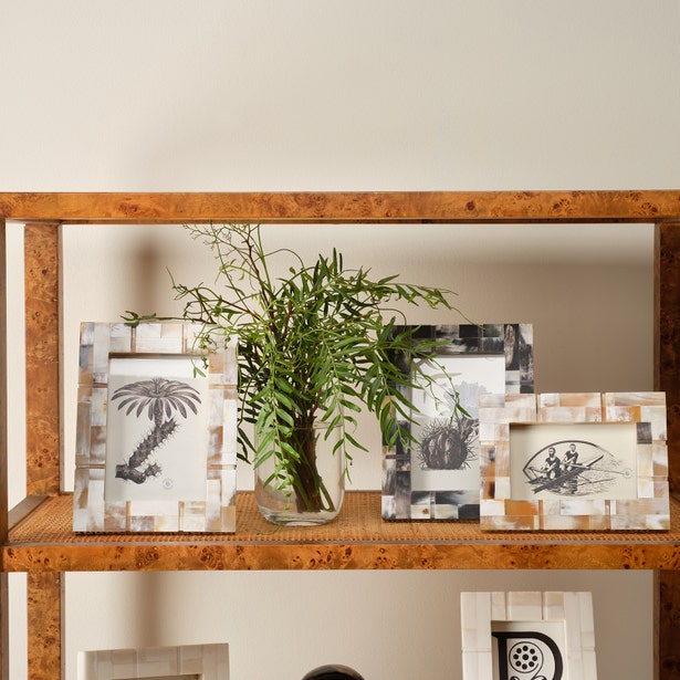 Decorative frames on a wooden shelf with a vase containing greenery.