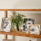 Decorative shelf with framed pictures and a vase with greenery on a neutral background