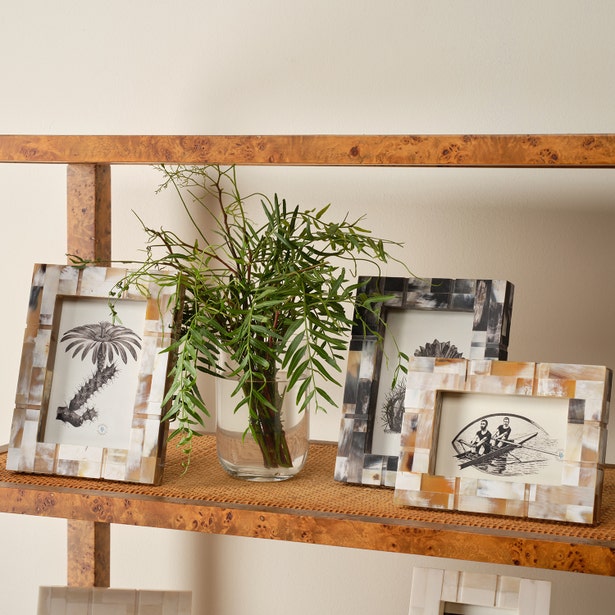 Decorative shelf with framed pictures and a vase with greenery on a neutral background