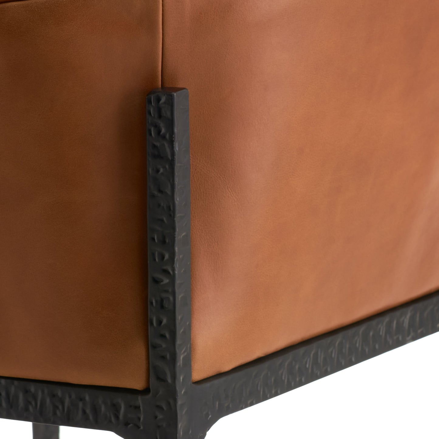 Close-up detail of a tan leather armchair corner with a textured black metal frame leg.