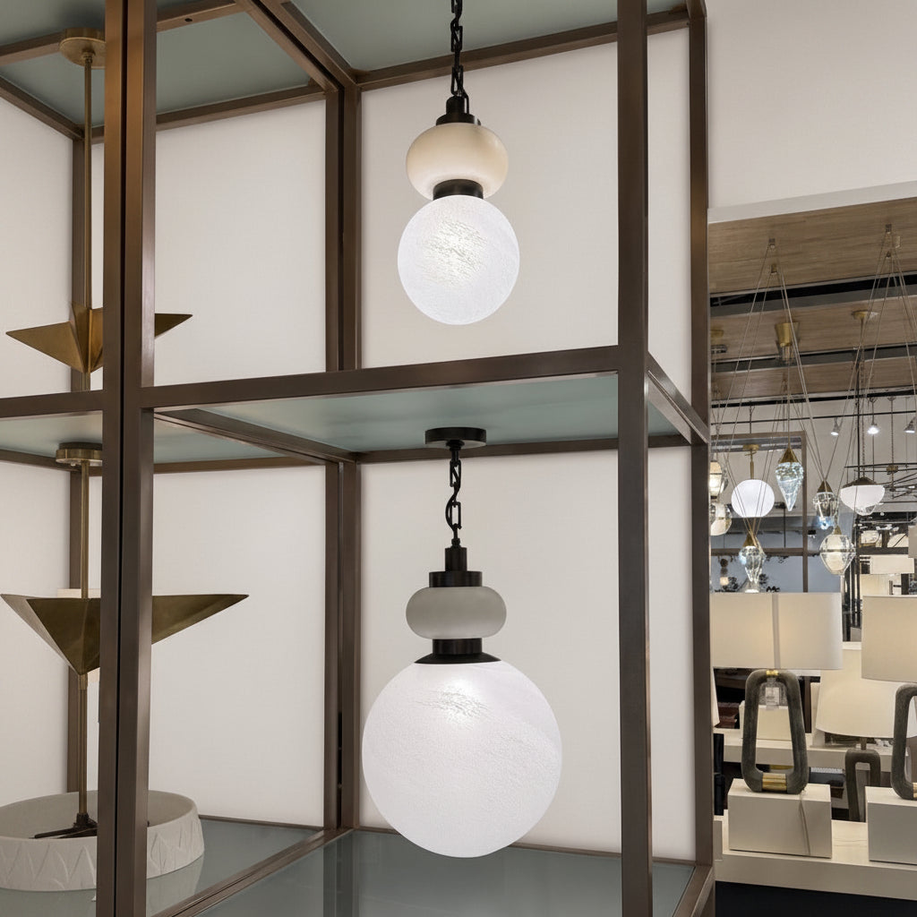 A modern pendant light fixture with a black metal chain and a multi-tiered spherical glass shade in frosted white and warm beige, shown hanging in a furniture showroom.