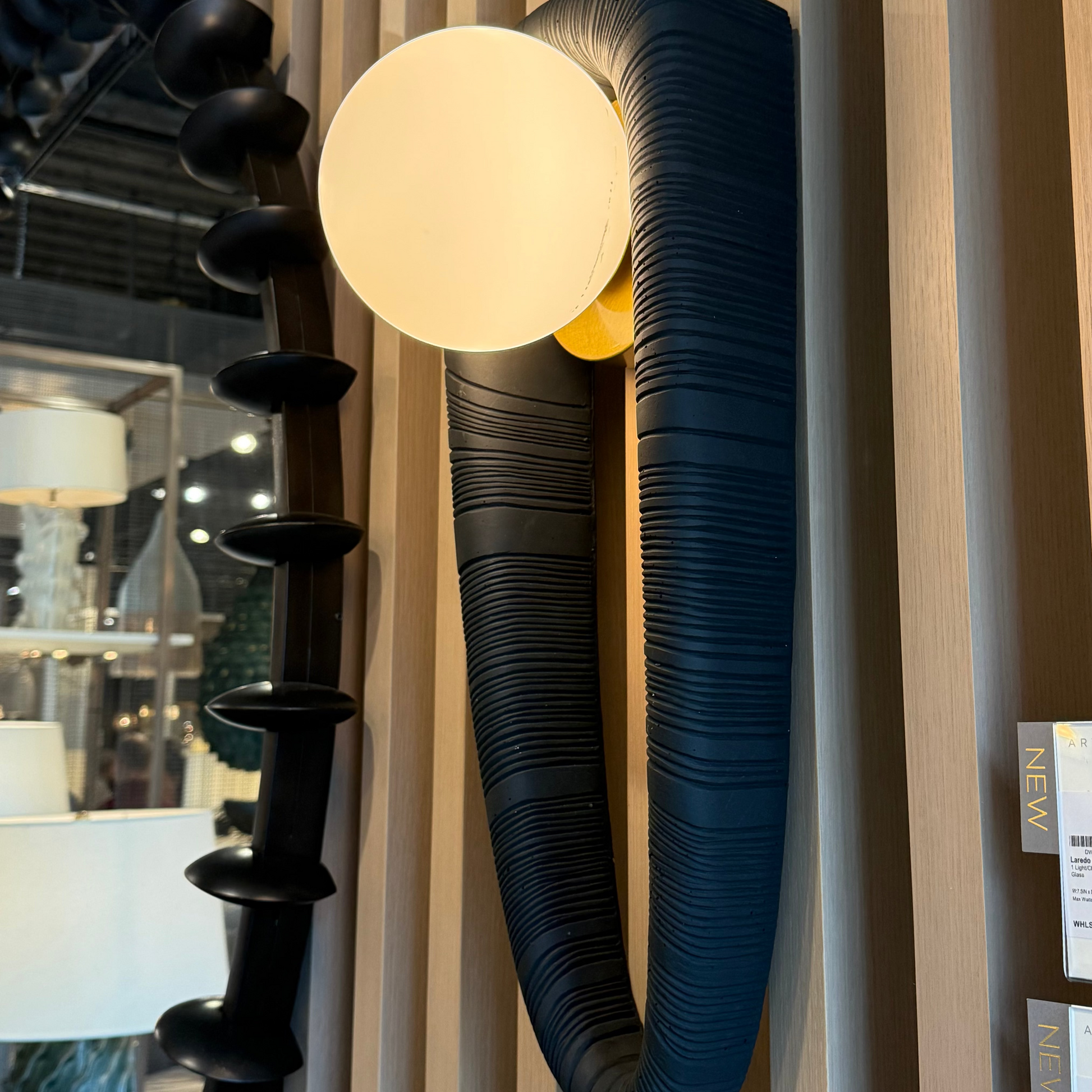Modern wall lamp with a black, ribbed design on a beige wall.