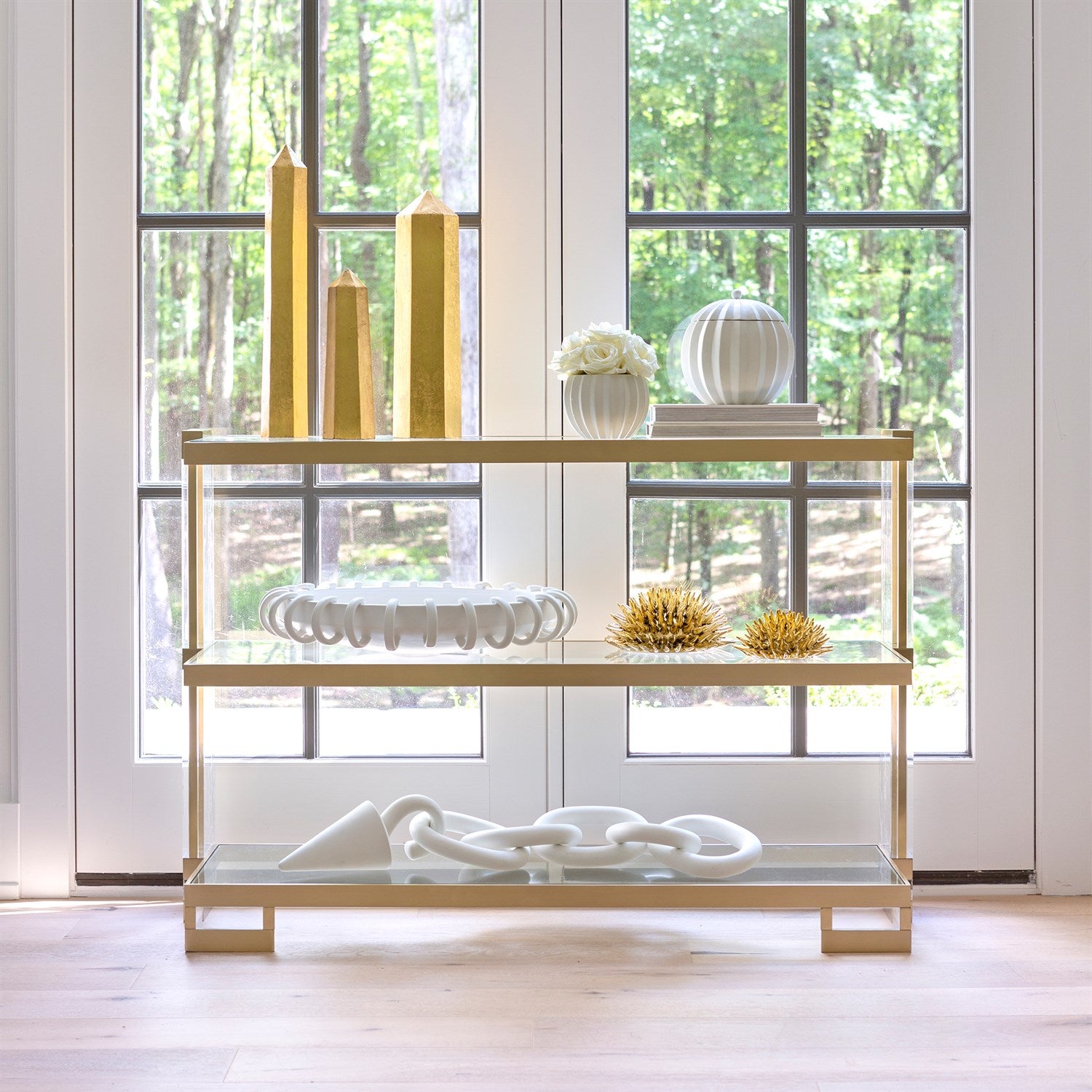 Gold console table with decorative items in a room with large windows.