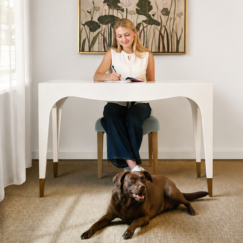 Woman sitting at a table with a dog lying on the floor in a home setting.