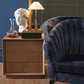 Wooden nightstand with decorative items next to a blue armchair against a dark wall.