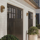 Pair of dark brown garage doors on a light brick wall with decorative lights.