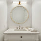 A white bathroom vanity with an integrated sink, brushed metal faucet, a round marble-framed mirror, and a wall-mounted rectangular light fixture above.