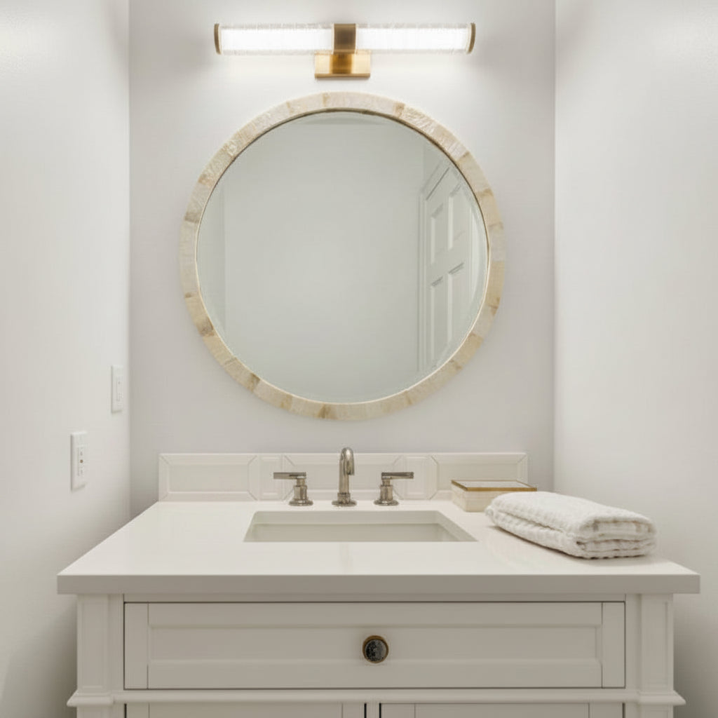 A white bathroom vanity with an integrated sink, brushed metal faucet, a round marble-framed mirror, and a wall-mounted rectangular light fixture above.