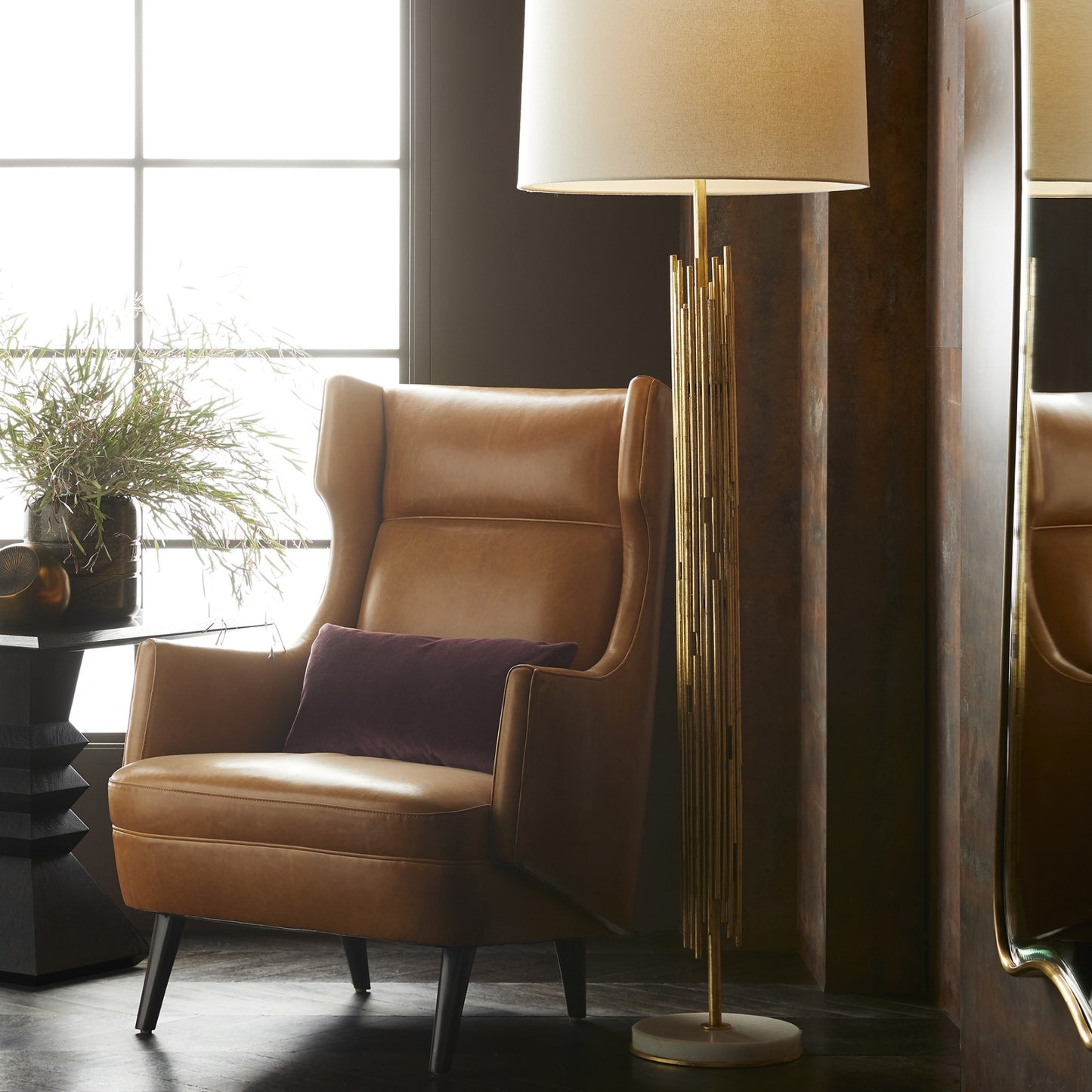 Brown leather armchair with a purple pillow next to a tall floor lamp in a room with large windows.