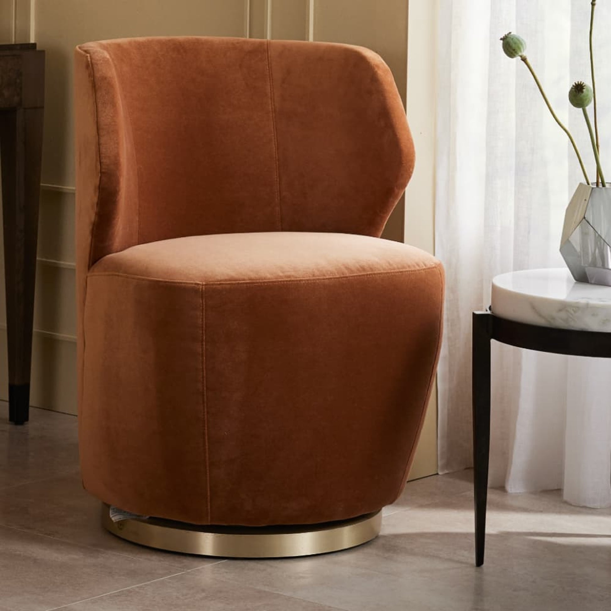 Brown velvet swivel chair in a room with a table and decorative elements.