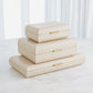Stack of beige jewelry boxes with gold accents on a white surface