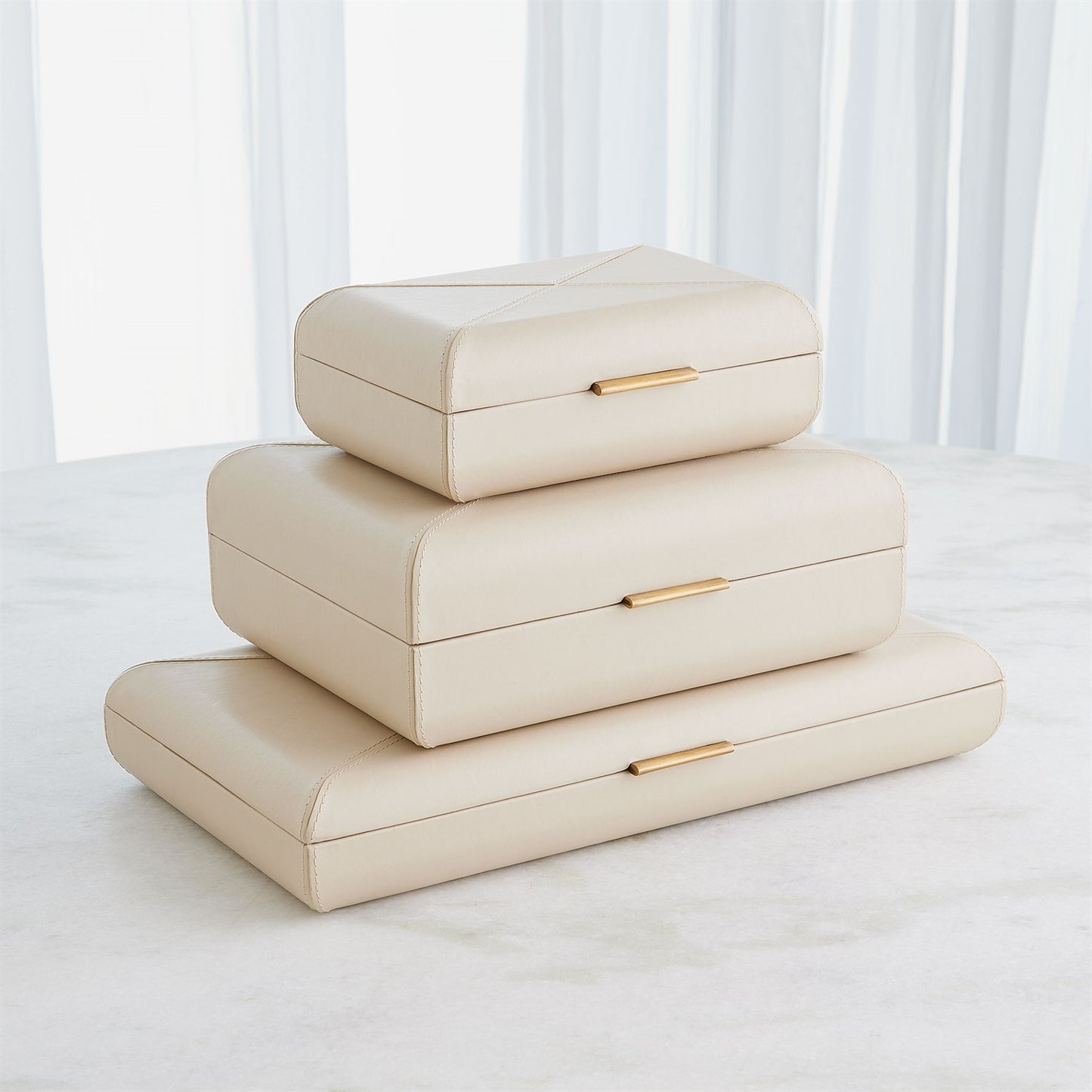 Stack of beige jewelry boxes with gold accents on a white surface