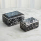 Two black marble boxes on a light gray surface with a white paneled background