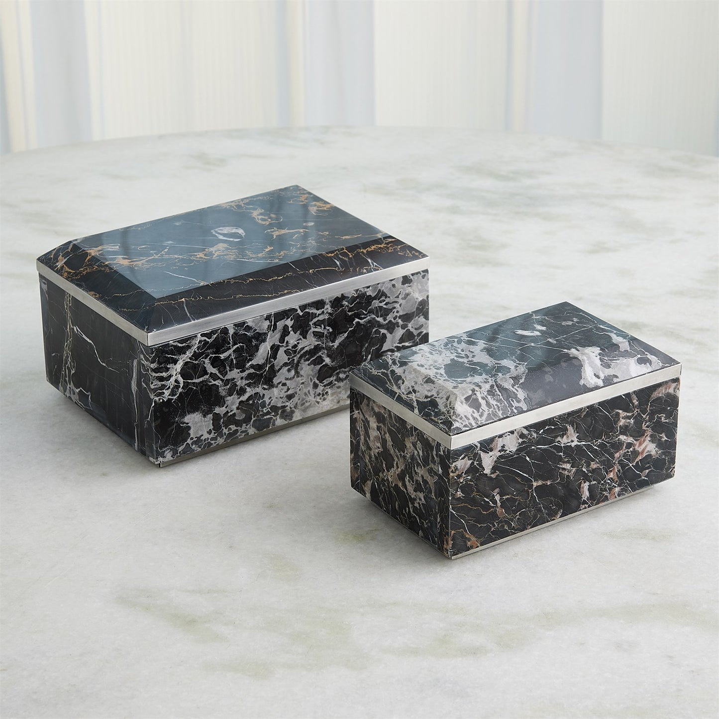 Two black marble boxes on a light gray surface with a white paneled background