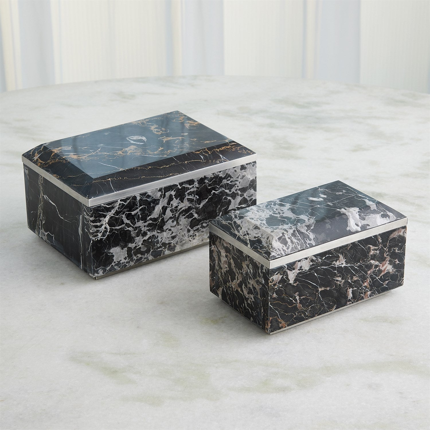 Two black marble boxes on a light gray surface with a white paneled background