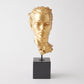 Gold-colored bust on a black pedestal against a white background