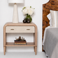 Wooden nightstand with decorative items next to a bed with a wooden headboard.