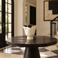 A round black marble dining table in a grand entryway, styled with a ribbed off-white ceramic vase with a black and white striped rim.