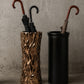 Two umbrella stands, one with a natural wood pattern and the other black, against a gray concrete wall.