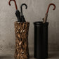 Two umbrella stands, one with a natural wood pattern and the other black, against a gray concrete wall.