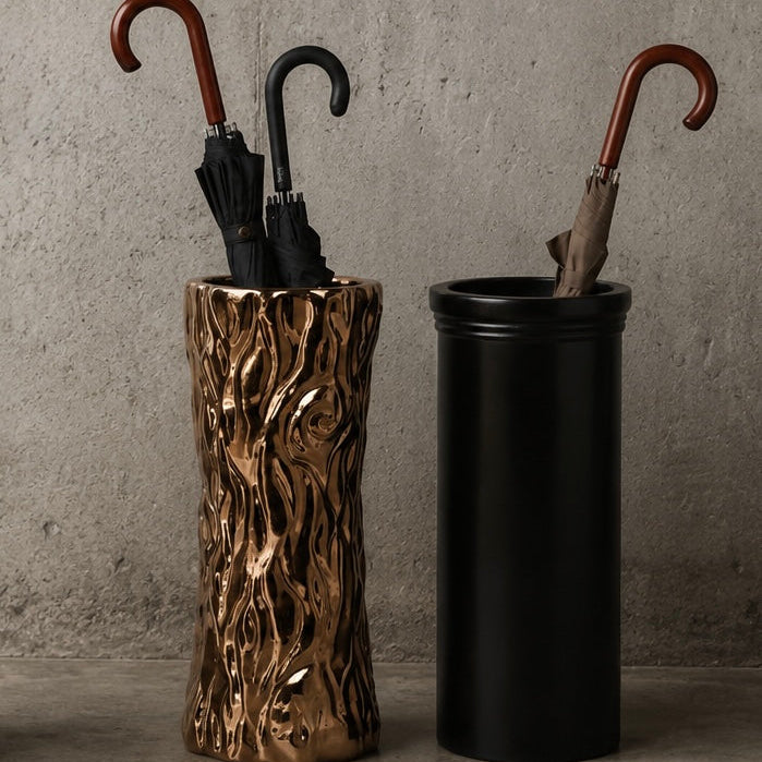 Two umbrella stands, one with a natural wood pattern and the other black, against a gray concrete wall.