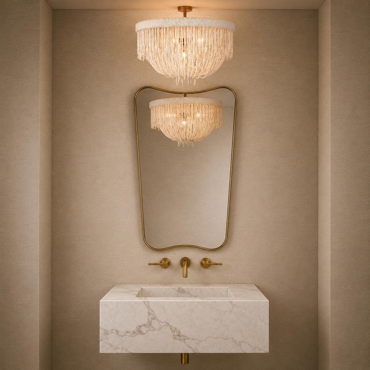 A modern bathroom vanity setup featuring a rectangular white marble sink with gold hardware, a large gold-framed mirror, and a matching gold-framed wall sconce reflecting the light. Above the mirror, a round gold-framed chandelier with a white fringed shade hangs against a warm beige textured wall.