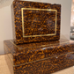 Tortoiseshell-patterned boxes with gold accents on a textured surface.