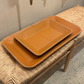 Two brown trays on a woven bench against a neutral wall.