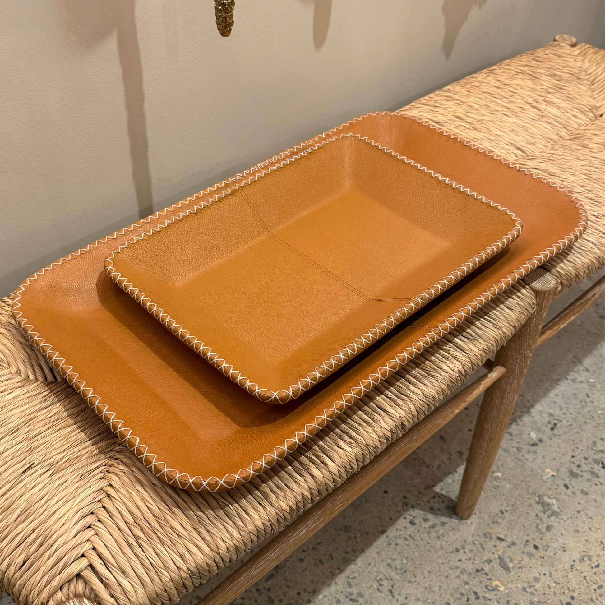 Two brown trays on a woven bench against a neutral wall.